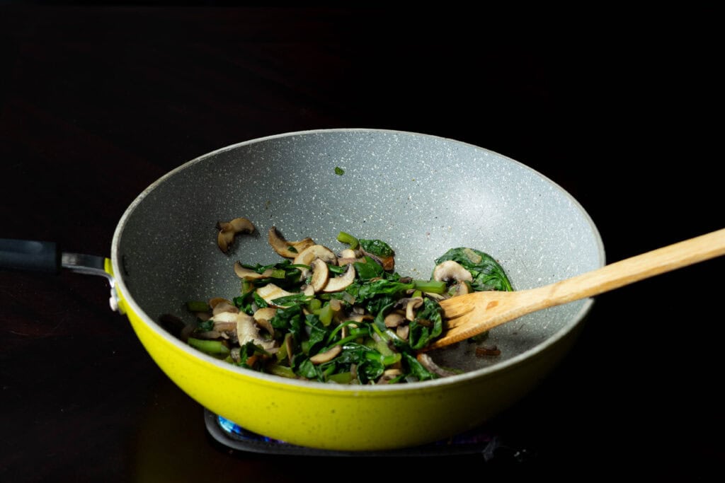 Large green pan with cooked veggies for the tofu scramble.
