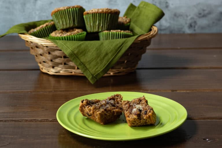 Small plate with buttered almond chocolate chip muffins, and basket of remaining muffins in the background.