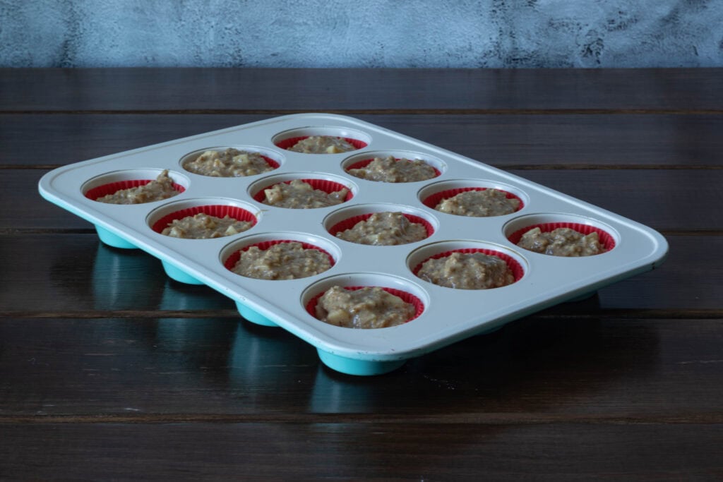 Apple cinnamon muffin batter evenly divided amongst lined-muffin tray.