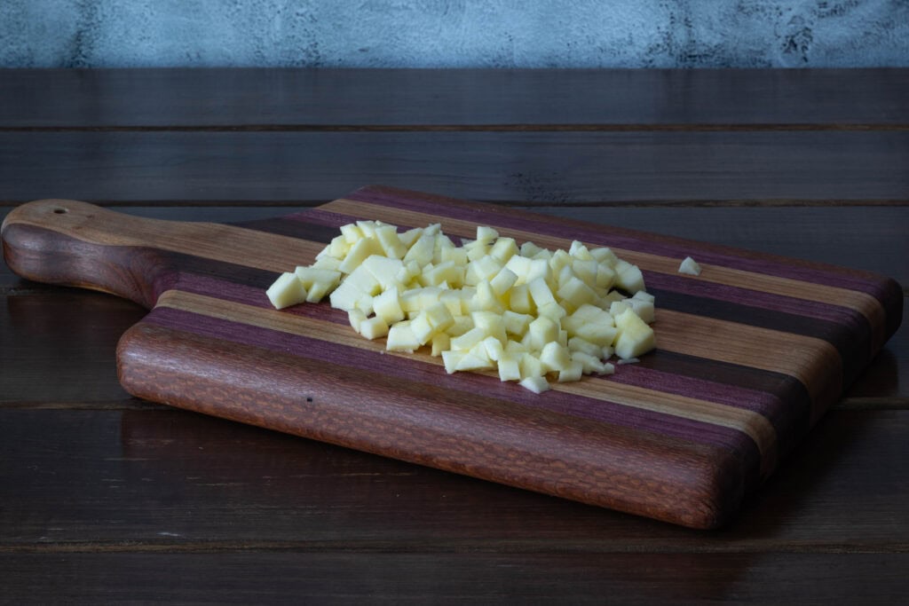 Peeled and diced apples sitting on a wooden cutting board.