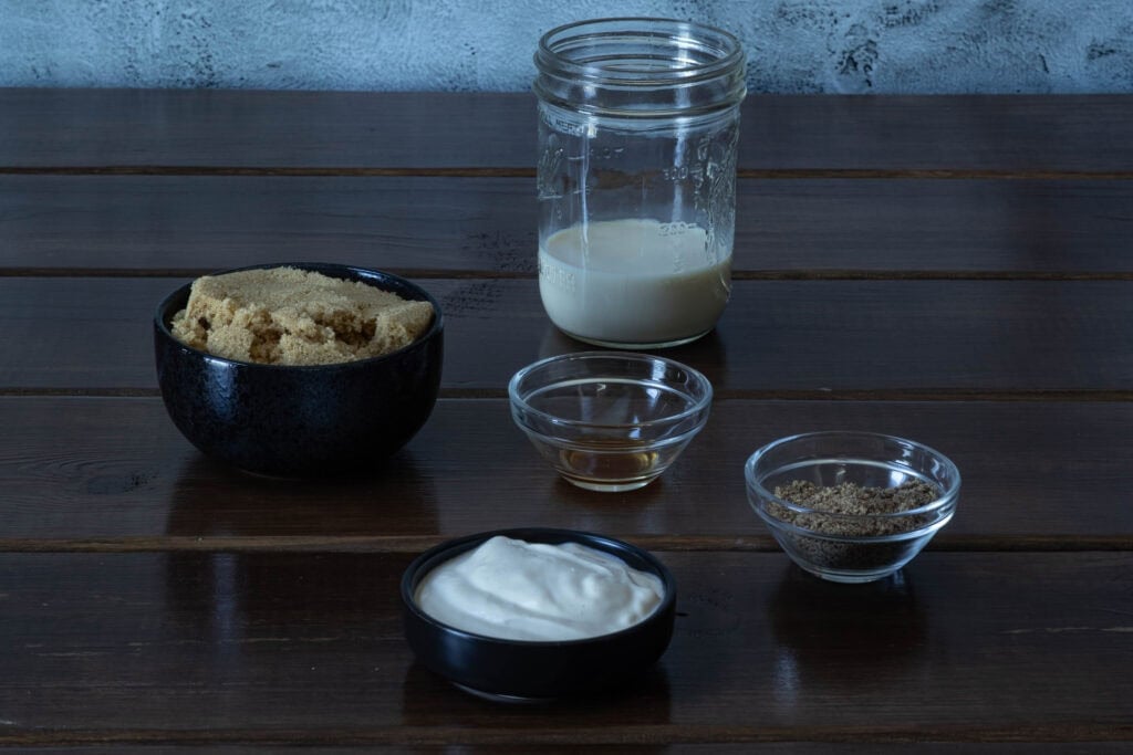 Apple Cinnamon muffin ingredients sitting on a wooden table - brown sugar, vegan yogurt, vanilla extract, ground flax seed and soy milk.