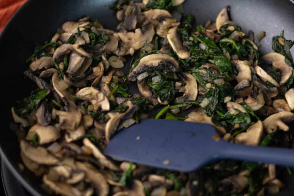 Cooked spinach and mushrooms in a pan.