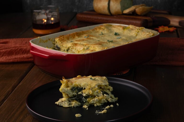 Plate with butternut squash lasagna, large casserole dish with remaining butternut squash lasagna in the background.