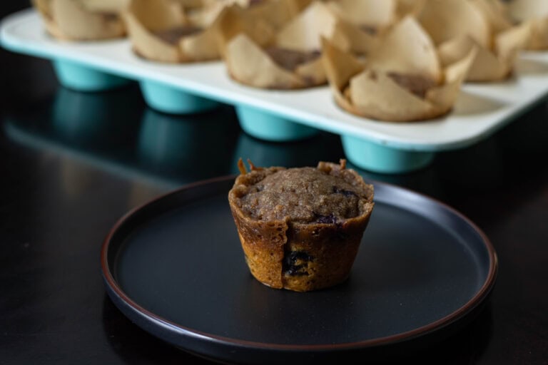 Blueberry Pumpkin Muffin sitting on a plate with a muffin tray in the background.