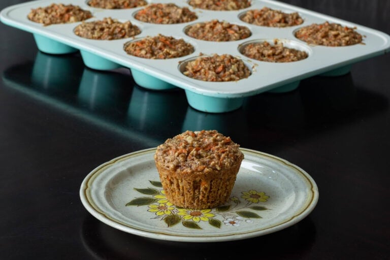 Carrot cake muffin sitting on a small plate with a muffin tin with remaining muffins in the background.