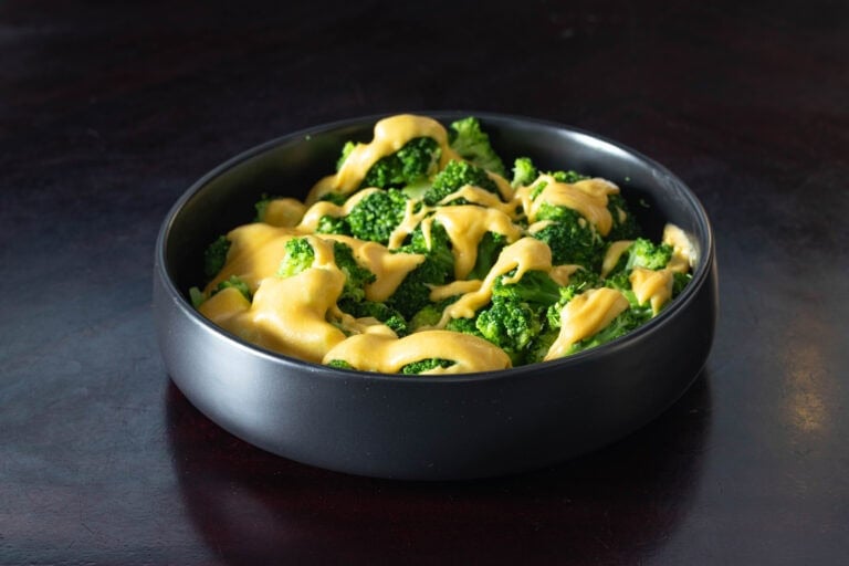 Large black bowl filled with freshly steamed broccoli covered in vegan cheese sauce.