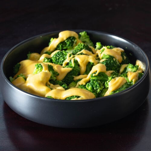 Large black bowl filled with freshly steamed broccoli covered in vegan cheese sauce.