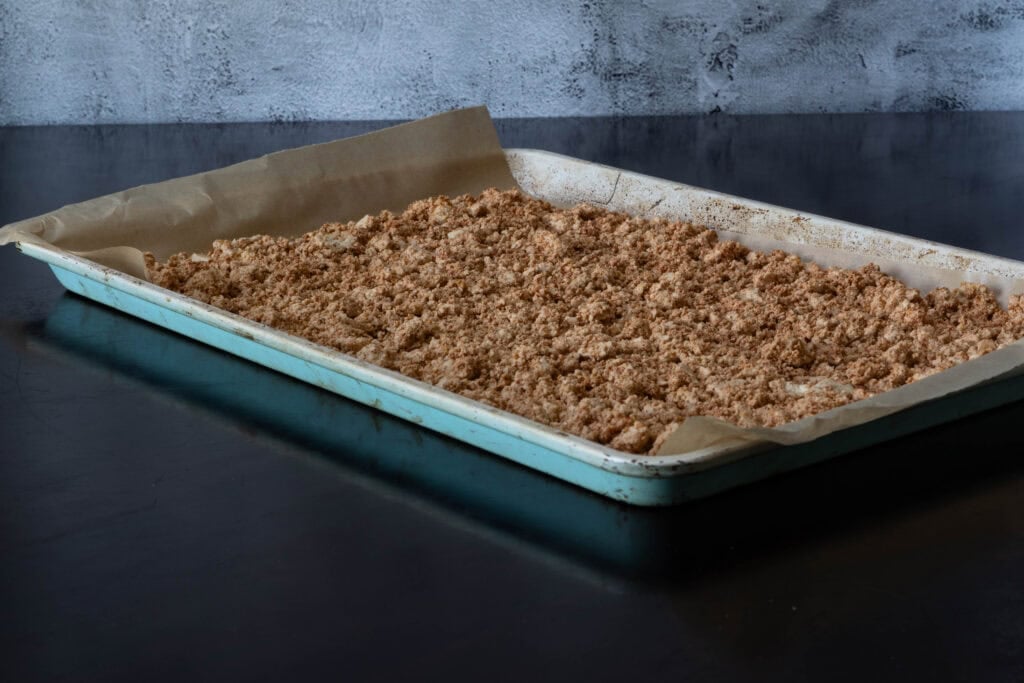 Seasoned and crumbled tofu spread out on a large parchment paper-lined baking sheet.