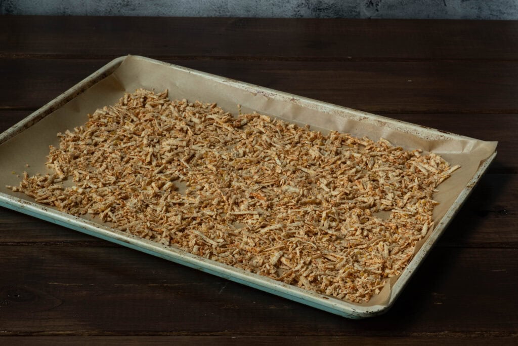 Parchment paper-lined baking sheet with uncooked, seasoned shredded tofu.