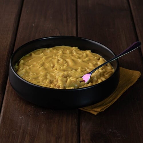 Upgraded vegan mac and cheese in a large black bowl sitting on a wooden table.