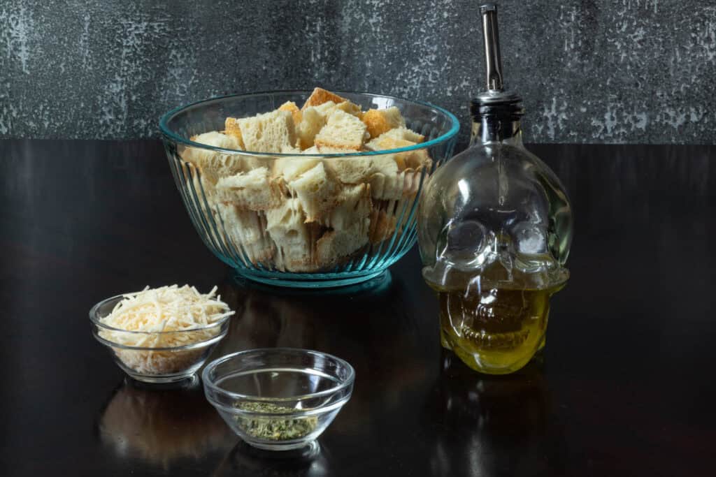 high protein crouton ingredients sitting on a table - bread chunks, olive oil, seasoning and vegan parmesan.