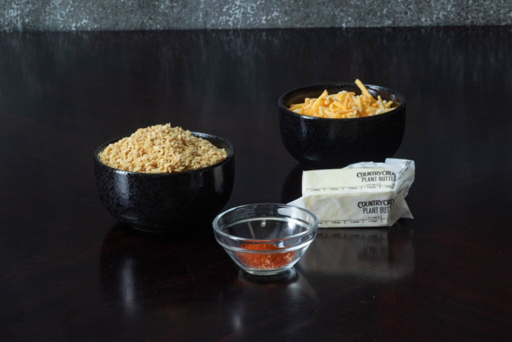 Topping ingredients for the high protein mac and cheese sitting on a wooden table - TVP, vegan butter, seasoning and vegan shredded cheese.