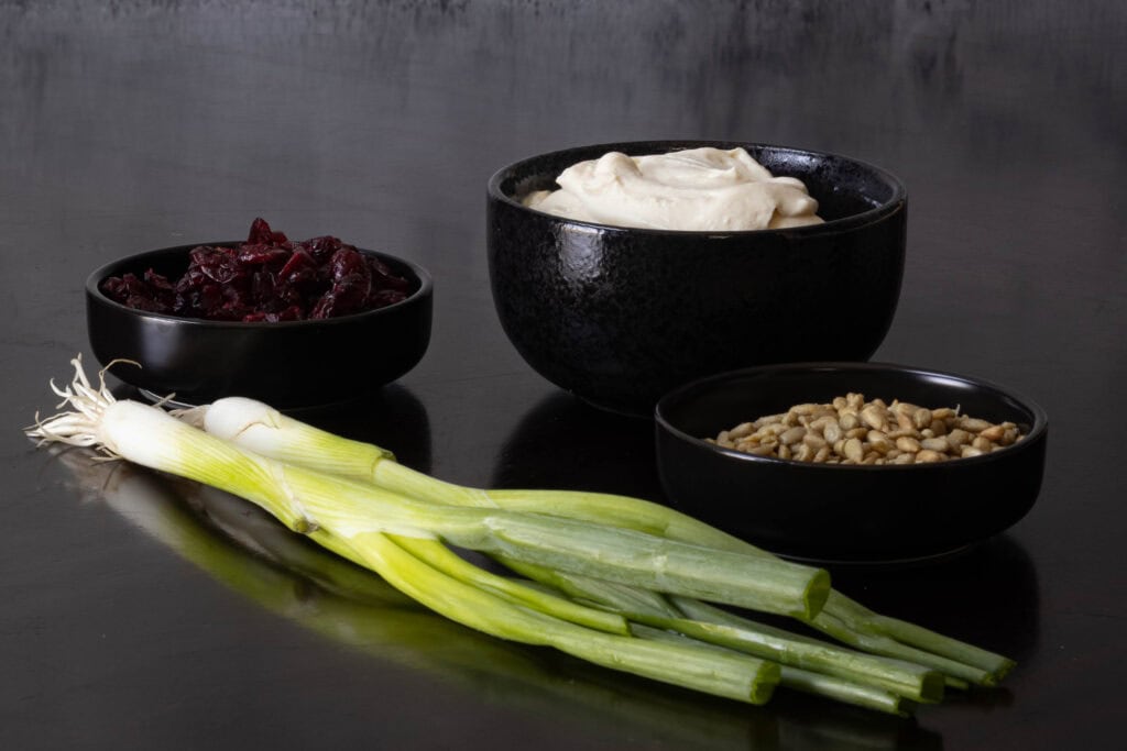 Holiday cream cheese dip ingredients sitting on a wooden table - craisins, vegan cream cheese, green onions and sunflower seeds.