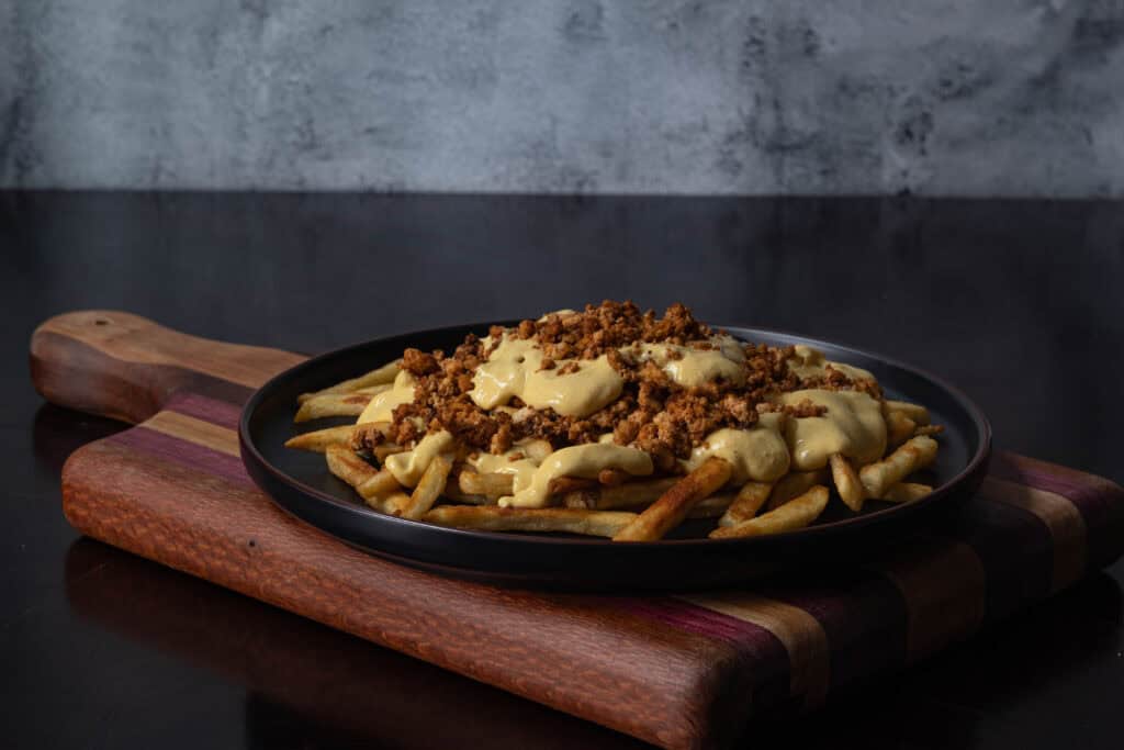 Plate of loaded fries topped with seasoned tofu crumbles and vegan cheese sauce.