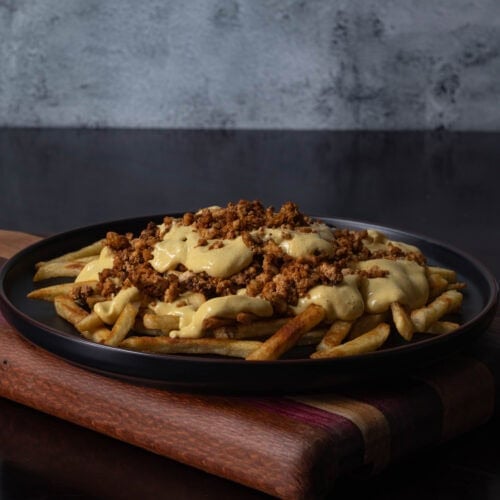 Plate of loaded fries topped with seasoned tofu crumbles and vegan cheese sauce.