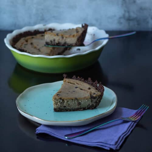 High Protein Peanut butter chocolate cheesecake sitting on a plate with a large pan with remaining cheesecake in the background.