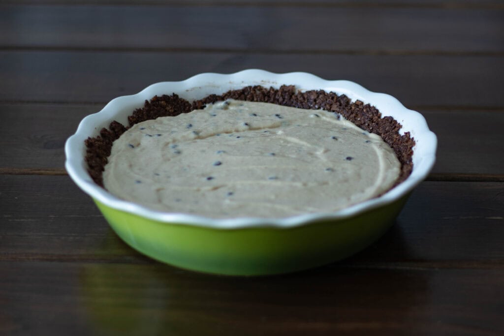 Uncooked peanut butter chocolate chip cheesecake sitting on a wooden table.