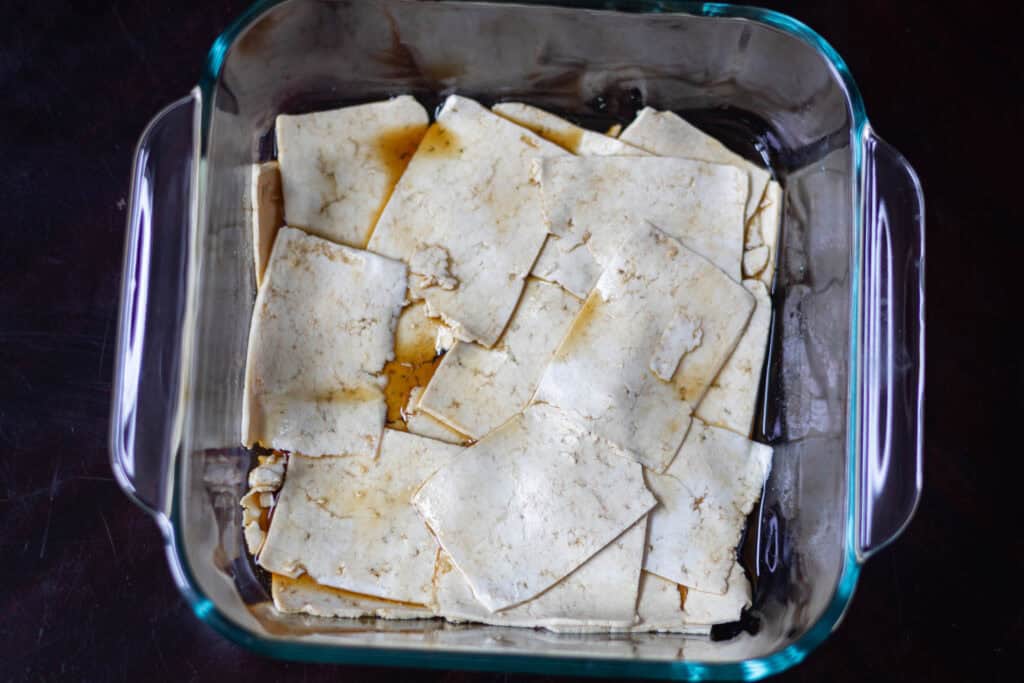 Thinly sliced tofu sitting in marinade in a small dish.