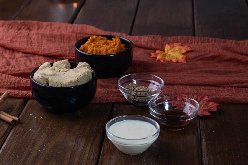 Pumpkin apple muffin ingredients sitting on a table - brown sugar, pumpkin puree, ground flax, vanilla, and soy milk.