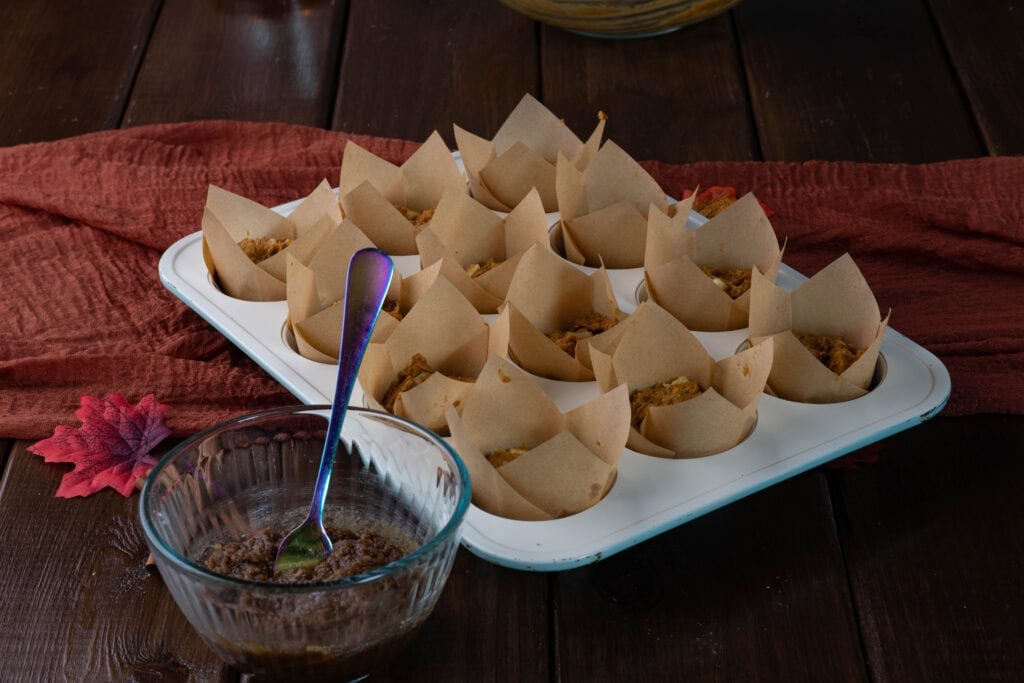 Pumpkin Apple Muffins in a muffin tin next to a bowl of the brown sugar topping.