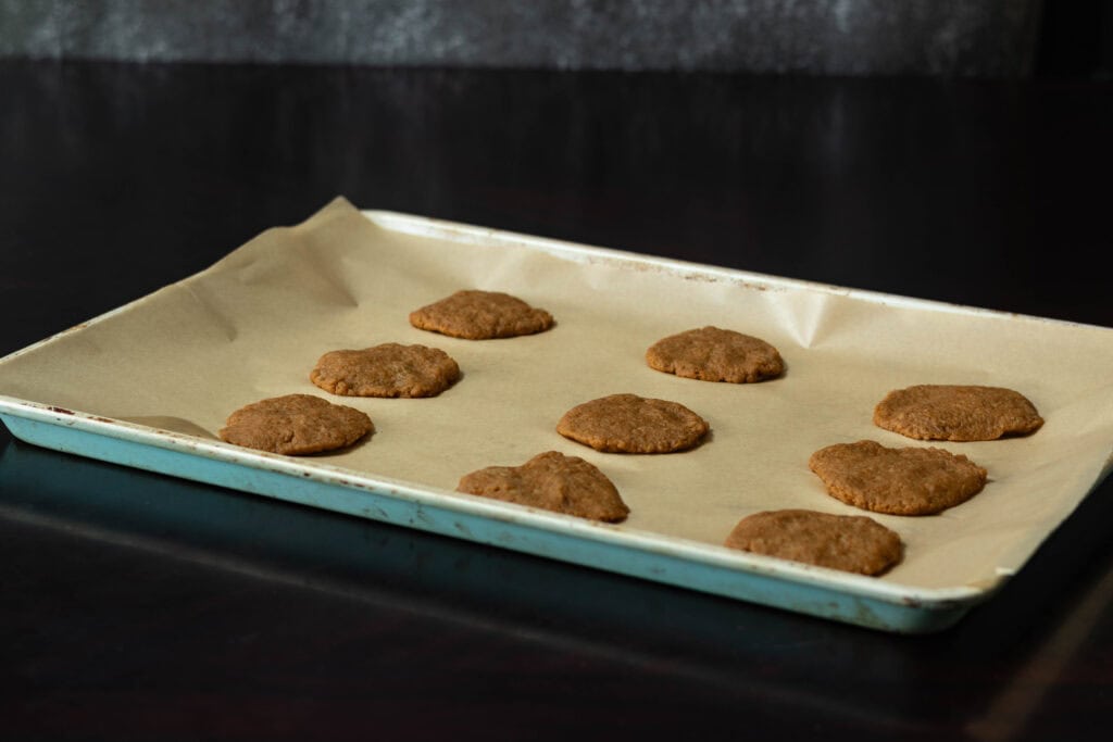 Large parchment paper-lined baking sheet with pumpkin seitan dough, shaped like cookies.