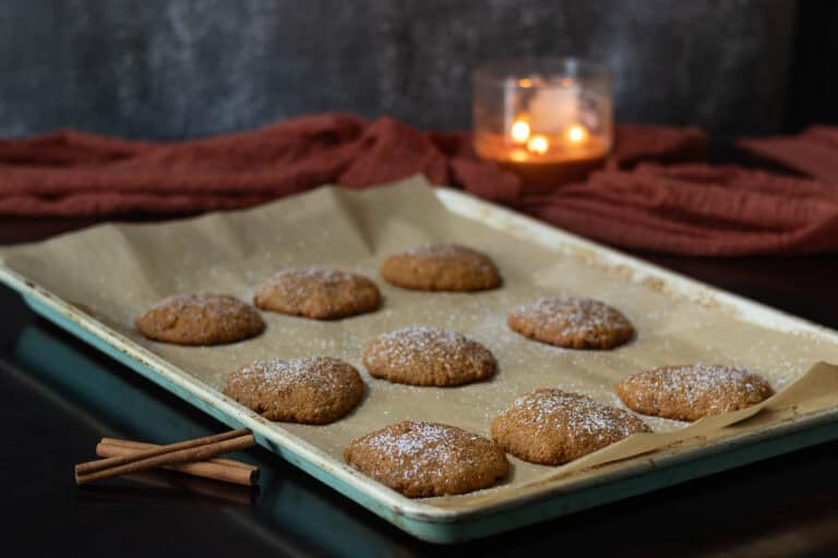Pumpkin Spice sietan sprinkled with powdered sugar sitting on a large parchment paper lined baking sheet. Area decorated with a fall scarf, three-wick candle and cinnamon sticks.