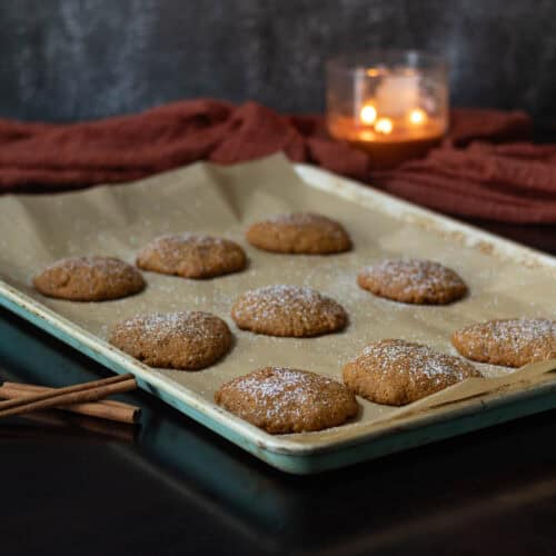 Pumpkin Spice sietan sprinkled with powdered sugar sitting on a large parchment paper lined baking sheet. Area decorated with a fall scarf, three-wick candle and cinnamon sticks.
