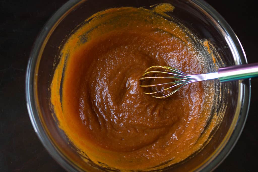 Wet ingredients for the pumpkin seitan mixed together in a large glass bowl. There is also a whisk in frame.