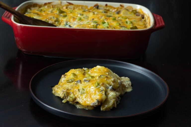 Vegan scalloped potatoes on a black plate with a casserole dish with the remaining scalloped potatoes in the background.