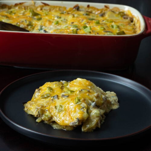 Vegan scalloped potatoes on a black plate with a casserole dish with the remaining scalloped potatoes in the background.