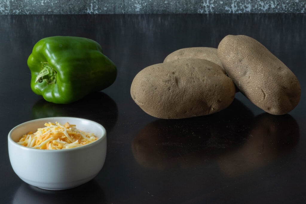Three large potatoes, a green bell pepper and shredded vegan cheese.