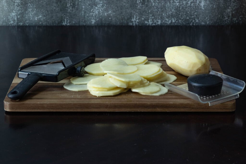 Cutting board with a mandolin, and sliced potatoes.