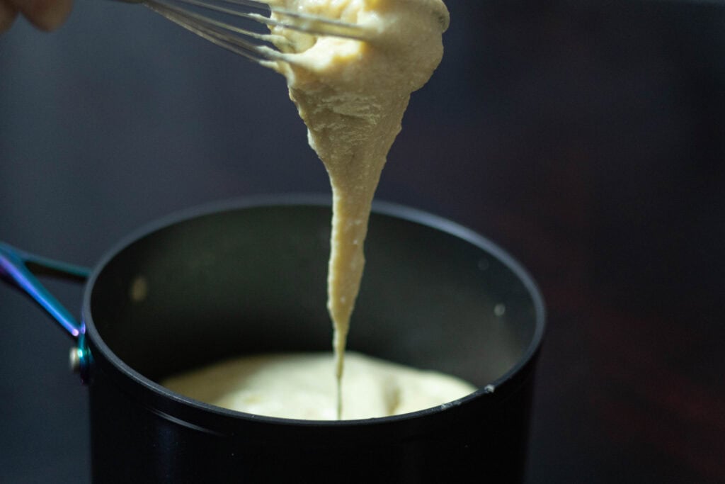 Stretchy soy mozzarella dripping off of a whisk into a sauce pan.
