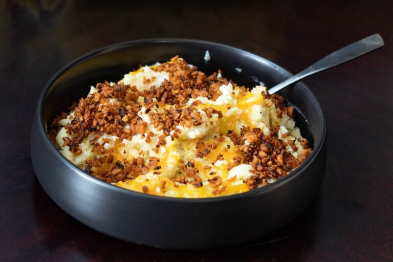 Large bowl with twice baked potato casserole topped with melted vegan cheese and crispy vegan bacon bits.