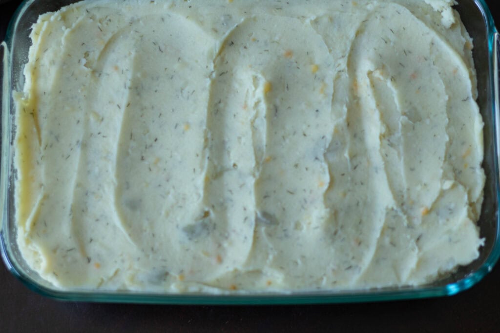 Large glass casserole dish with potato mixture, uncooked.
