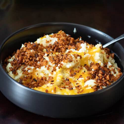 Large bowl with twice baked potato casserole topped with melted vegan cheese and crispy vegan bacon bits.