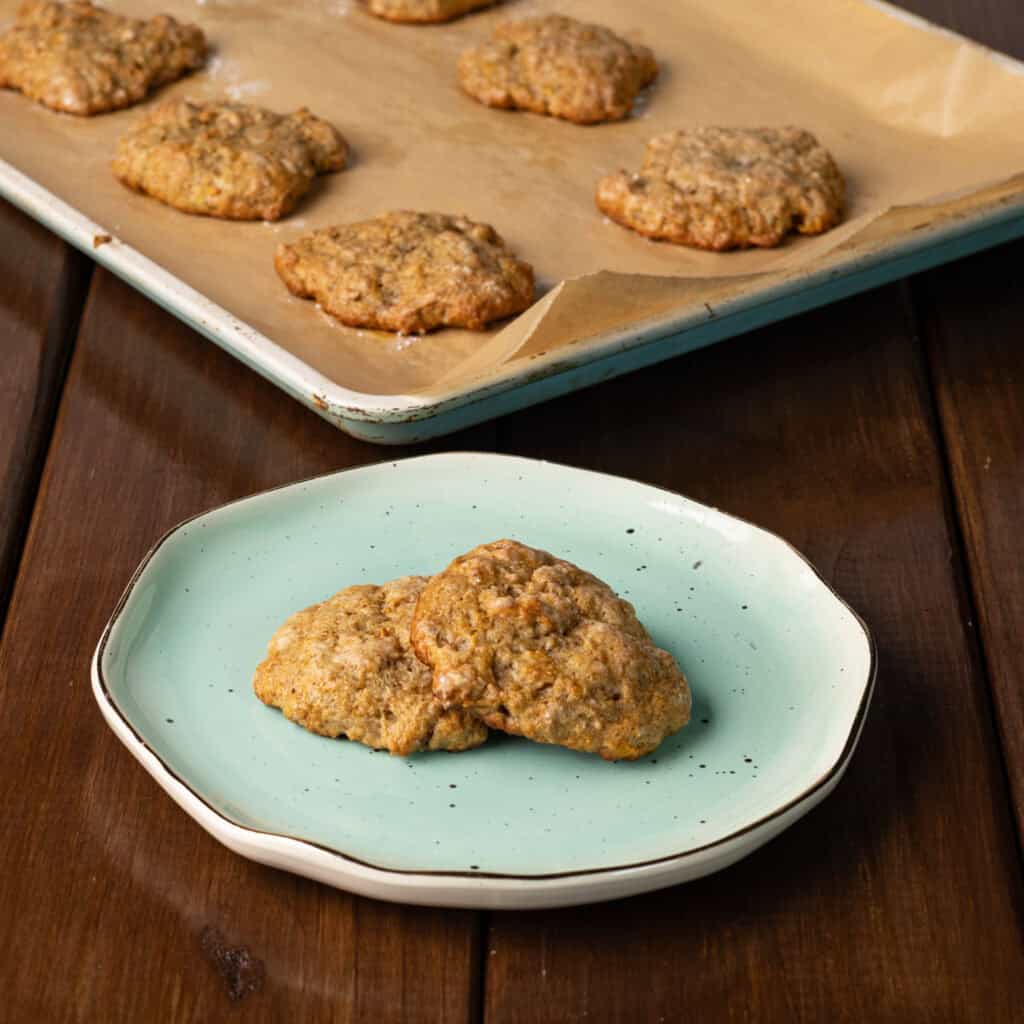 Banana Bread Seitan Cookies on a plate and a parchment paper-lined baking sheet.