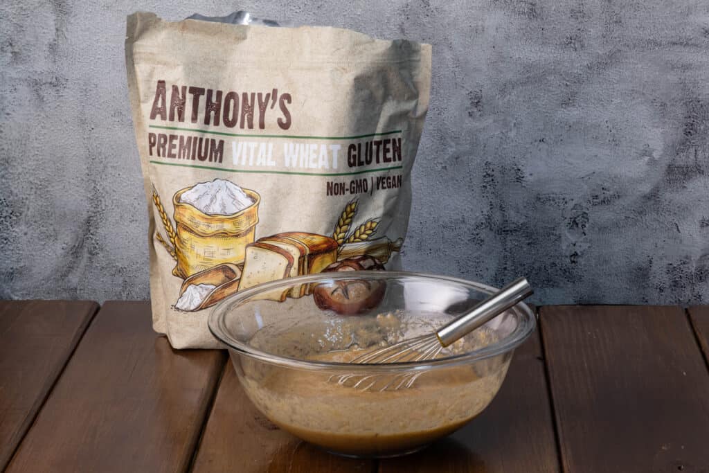 Wet ingredients for banana bread seitan mixed in a glass bowl with a bag of vital wheat gluten in the background.