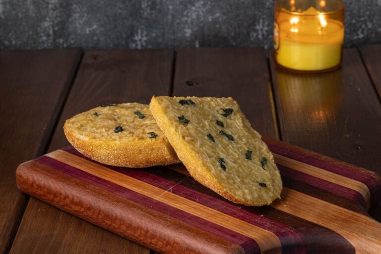 Two pieces of garlic bread sitting on a wooden cutting board.