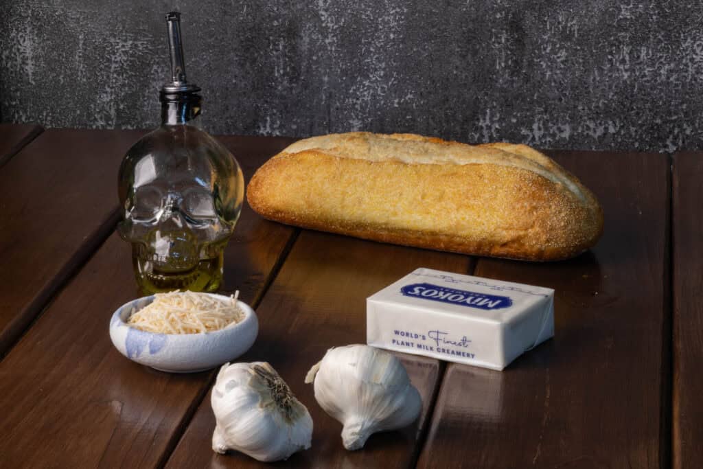 Garlic bread ingredients - bread, olive oil, vegan parmesan, vegan butter, and garlic.