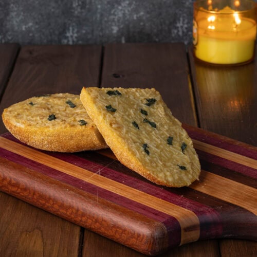 Two pieces of garlic bread sitting on a wooden cutting board.