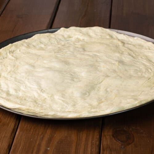 Pizza dough on a large pizza pan.