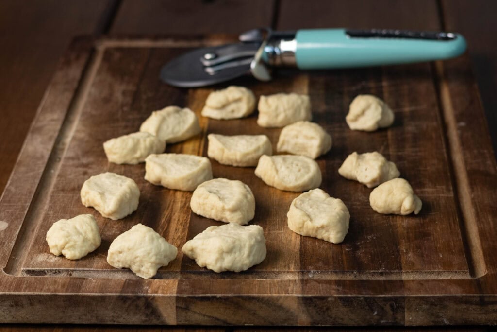 Cut pieces of pretzel bite dough on a wooden cutting board.