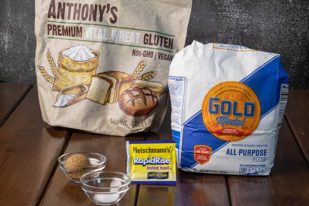 Ingredients for the high protein pretzel bites sitting on a wooden table - vital wheat gluten, flour, salt, brown sugar and instant yeast.