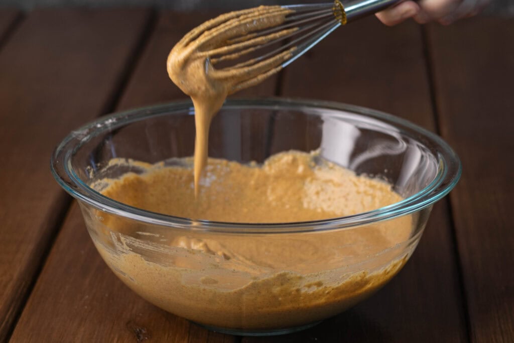 Pancake batter dripping from whisk in a large glass bowl.