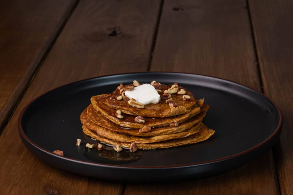 High protein pancakes topped with syrup, chopped pecans and a pad of butter.