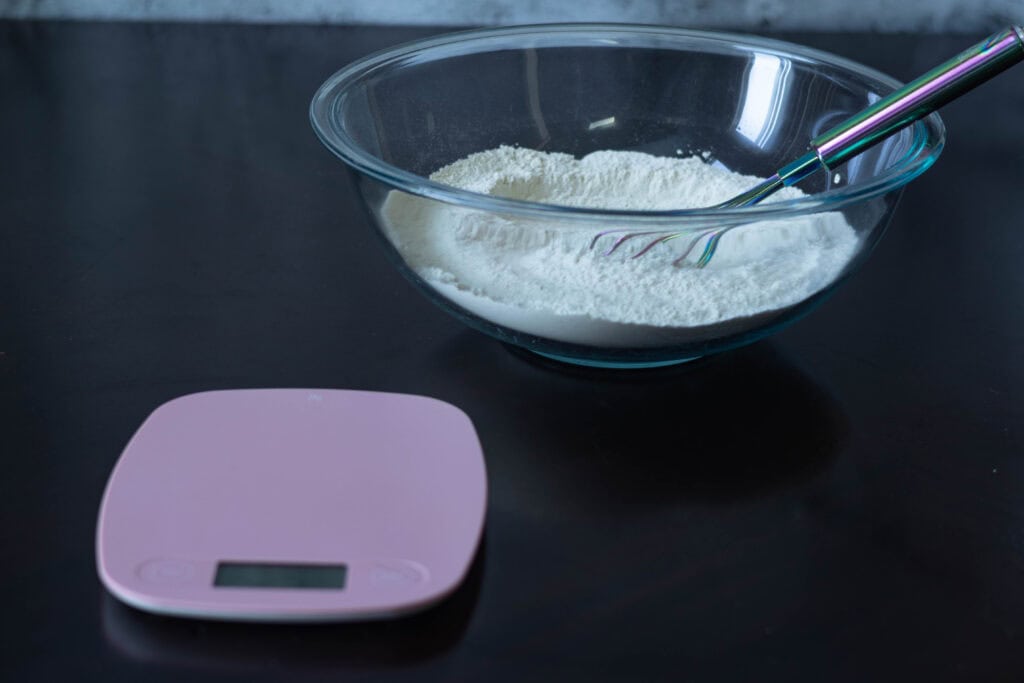 Bowl of whisked flour sitting next to a kitchen scale.