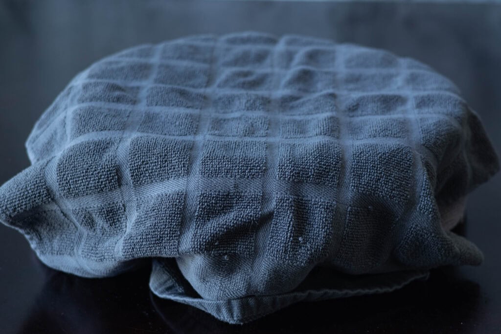 Pizza dough in a bowl covered in kitchen towels.