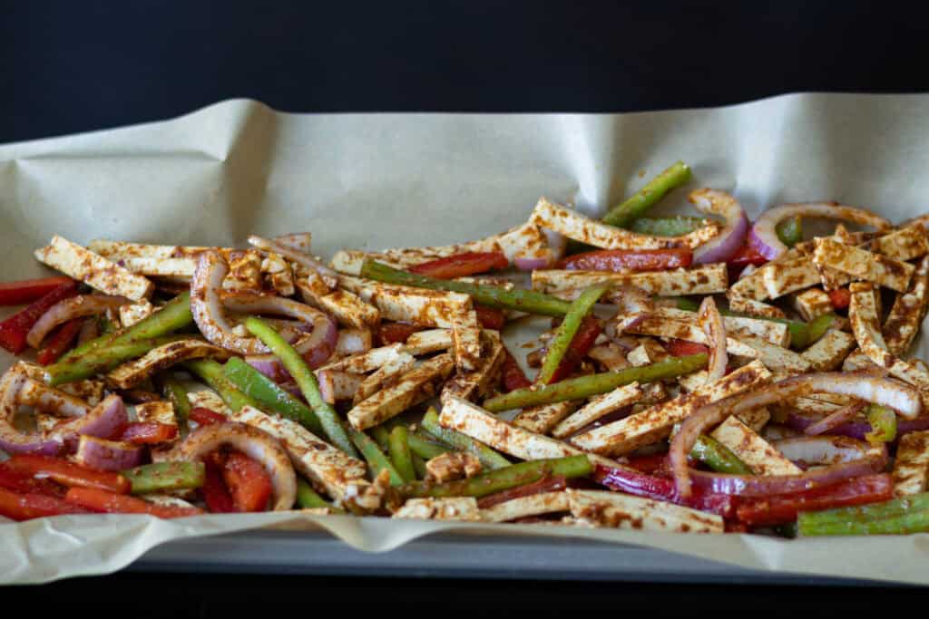 Seasoned tofu fajita ingredients on a parchment paper-lined baking sheet.