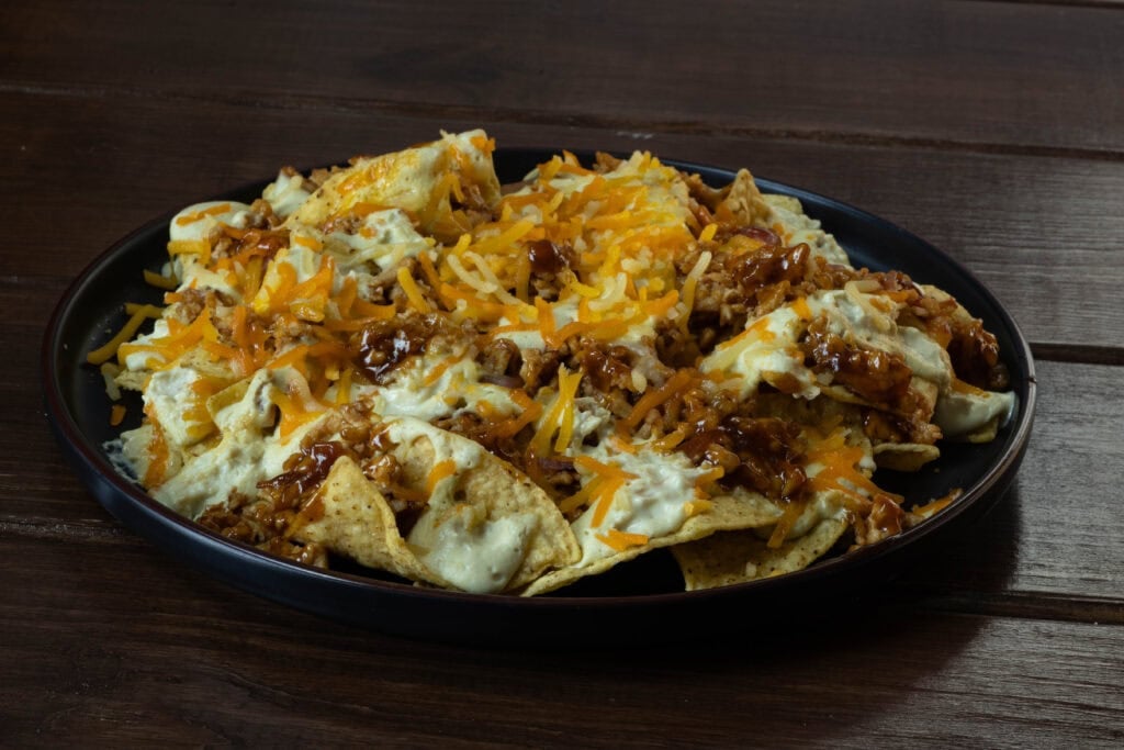 Plate of loaded nachos with shredded BBQ tofu, vegan cheese, and cashew queso.
